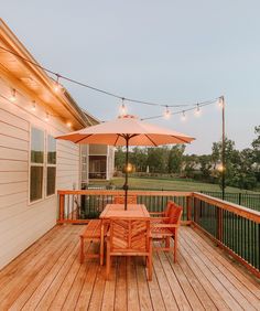 an umbrella is on top of a wooden deck with string lights and chairs around it