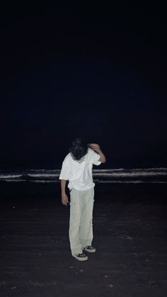 a man standing on top of a beach next to the ocean under a dark sky