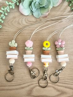 four keychains with flowers on them sitting next to a flower pot and succulents