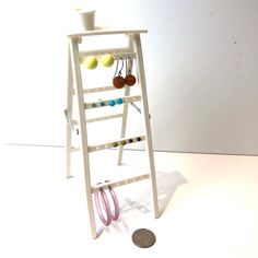 a small white ladder with earrings hanging from it's sides next to a coin