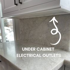 the under cabinet electrical outlets are in white cabinets and marble counter tops with an arrow symbol on it