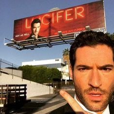 a man is pointing to the left side of his face while standing in front of a billboard