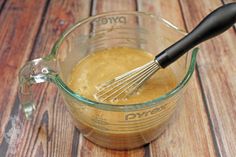 a whisk in a glass measuring cup on a wooden table with brown liquid