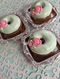 there are four donuts with frosting and pink flowers on them in the tray