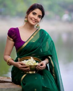 a woman in a green sari is holding a bowl of flowers and smiling at the camera