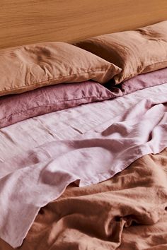 an unmade bed with several pillows and blankets on it's sides, all in different colors