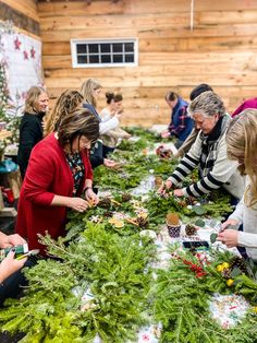 a group of people standing around a table covered in christmas wreaths and pine cones