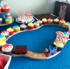 a table topped with cupcakes and cakes next to a train on the track