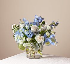 a glass vase filled with blue and white flowers on top of a table next to a wall