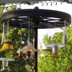 several bird feeders are hanging from a wooden gazebo in the sun with trees in the background