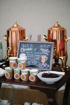 a table topped with coffee cups next to a chalkboard sign that says hot chocolate