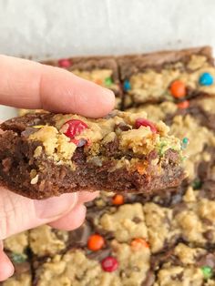 a hand holding up a cookie bar with m & m cookies on the top and chocolate chips on the bottom