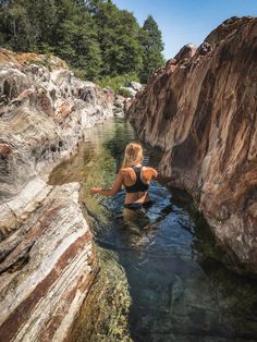 a woman is wading in the water near some rocks