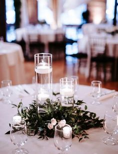 the centerpiece is surrounded by candles and greenery on top of a white table cloth