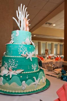 a three tiered cake decorated with sea creatures and corals on a table in a banquet room