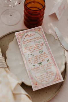 a menu sitting on top of a white plate next to a glass filled with wine