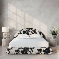 a white bed with black and white pillows in a room next to a plant on the floor