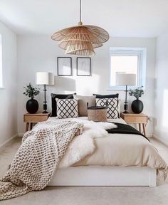 a bed with pillows and blankets on top of it next to two lamps hanging from the ceiling