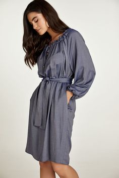 This belted dress is crafted in blue denim style woven viscose fabric. It has a wide round neckline with an internal tie allowing either for ruching or an off-shoulder look. The tie is in the same fabric with metal stoppers at the ends. There is a V opening below the neckline. It has long raglan sleeves with elastic at the cuffs creating gathers. There is an inseam pocket on either side. The dress can be worn without the belt for a sack silhouette. The belt is included. Gentle machine wash. Turn garment inside out. Cold water. Mild detergent. Iron on reverse side. Do not tumble dry. Do not bleach. Casual Blue Dresses With Tie Fastening, Casual Blue Dress With Tie Fastening, Elegant Belted Denim Dress, Elegant Denim Daywear Dress, Elegant Denim Dress For Daywear, Chic Blue Dress With Belted Cuffs, Blue Midi Dress With Belted Cuffs, Blue Tie Fastening Dress For Daywear, Blue Daywear Dress With Tie Fastening