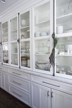 a white china cabinet with glass doors and shelves filled with dishes on top of it