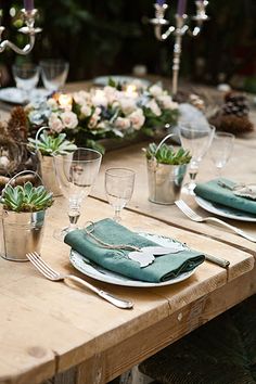 a wooden table topped with green napkins and silver cups filled with succulents