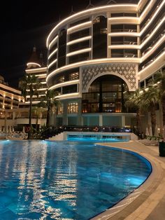 an empty swimming pool in front of a large building at night with lights on it