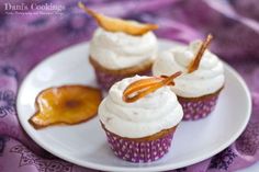 three cupcakes on a white plate topped with whipped cream and fruit toppings