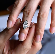 a woman's hand holding an engagement ring with a diamond in the middle, on top of her finger