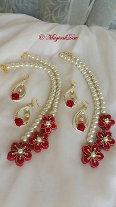 a necklace and earring set with red flowers on white pearls, sitting on a bed