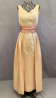 "Vintage 1960s formal in lovely pink and gold on cream brocade.  it is really two dresses in one as it is a long fitted sheath with a separate full overskirt plus cumberbund / sash.  Dress is sleeveless with a scoop neck that is lower in back, side zipper and long back kick pleat.  Skirt is set to a narrow waist band that fastens to dress with hooks and eyes.  It gathers across the back, wrapping part way over the front ending in soft pleats. The rose satin sash has no fastenings -- fold it over Elegant Brocade Dress For Occasion Wear, Fitted Brocade Evening Dress For Formal Occasions, Formal Fitted Brocade Evening Dress, Brocade Dresses With Fitted Bodice For Evening, Formal Floor-length Brocade Dress, Gold Brocade Dress For Gala, Formal Fitted Brocade Gown, Fitted Brocade Gown For Formal Occasions, Formal Brocade Gown With Fitted Bodice