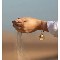 a person holding sand in their hand with a gold ring on it's wrist