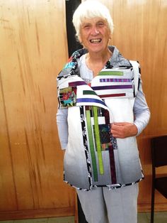 an older woman holding up a piece of art made out of paper and cloths