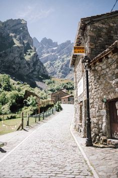 an old cobblestone street with mountains in the backgrouds and a yellow sign on it