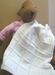 a crocheted teddy bear wrapped in a blanket sitting on the floor next to a wall