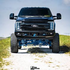 the front end of a black pickup truck on a dirt road with grass and blue sky in the background