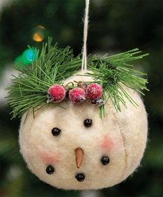 a snowman ornament hanging from a tree with berries and pine needles on it