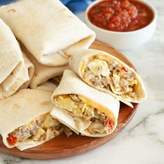 several burritos sitting on a plate with salsa in the background