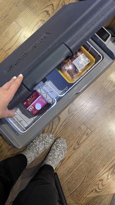 someone is holding their cell phone in an open storage compartment on the floor next to a wooden table