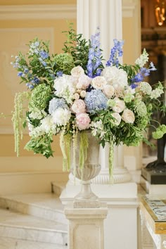 a vase filled with lots of flowers sitting on top of a white table next to a pillar