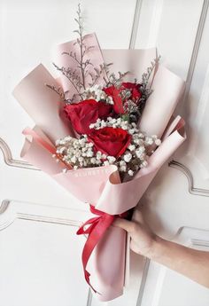 a person holding a bouquet of flowers in their hand on a white door with red ribbon