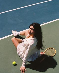 a woman sitting on the ground with a tennis racket and ball in her hand