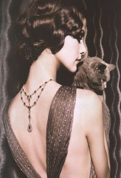 a woman in a dress holding a cat with her back turned to the camera,