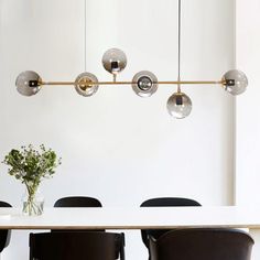 a dining room table with black chairs and a white wall in the background is an oval light fixture hanging over it