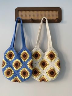 two crocheted purses hanging from hooks on a white wall, one blue and the other brown