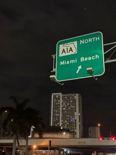 a green street sign hanging from the side of a metal pole over a city at night