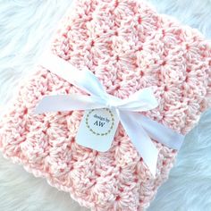 a pink crocheted blanket with a white ribbon on it and a tag that says,