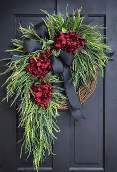 a wreath with red carnations and greenery hangs on a black front door