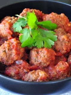 meatballs with tomato sauce and parsley in a black bowl on a blue cloth