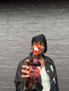 a man is drinking from a bottle in front of a brick wall and wearing a bandana