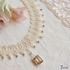 a necklace with pearls and beads on top of a white table cloth next to flowers